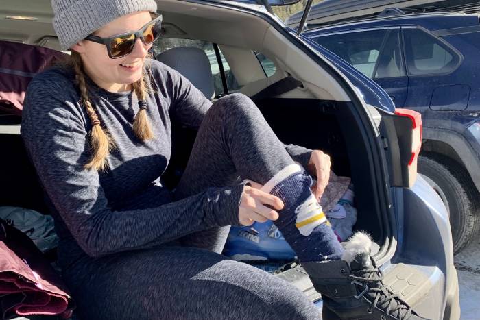 editor Mary Murphy wearing the REI baselayers putting on ski socks at the car