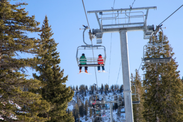 two skiers on a 3 person chairlift on a sunny day