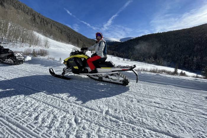 author sitting on a snowmobile, parked mid-ride on a bluebird day