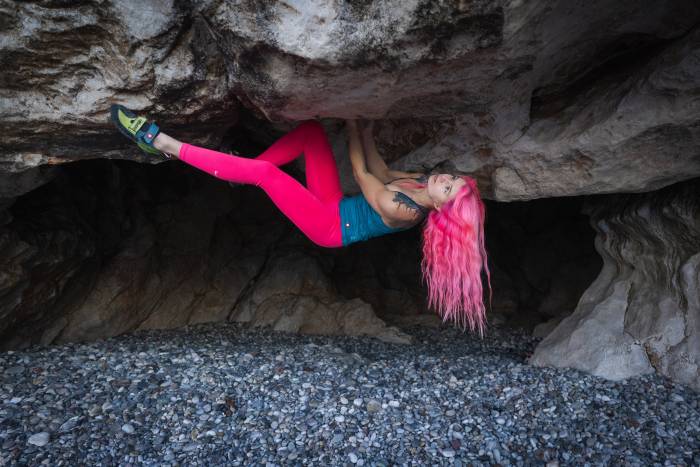 woman with pink hair bouldering in a cave