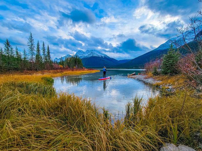 A person stand up paddle boarding on an alpine lake with mountains in the background.