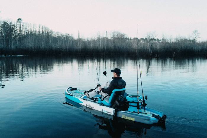 Person sitting on a stand up paddle board pedaling on the water with gear attached to the board.