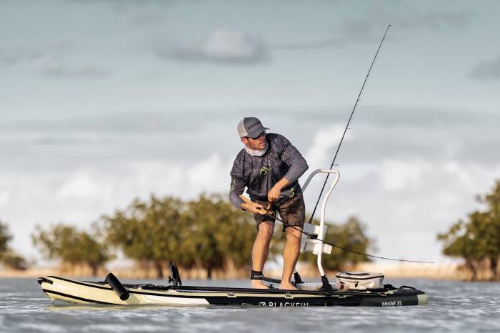 Person with a hat reeling in a fish from an iRocker stand up paddle board on the water.