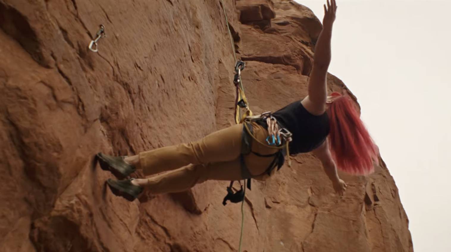 a female climber with bright pink hair hanging off a rope with her arms outstretched