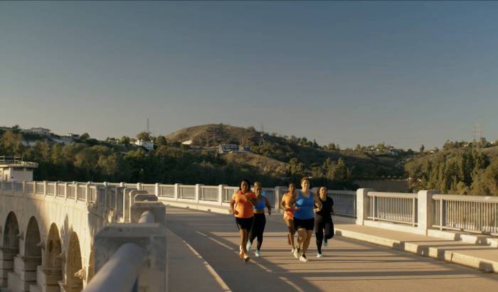 a pack of four female Black runners job over a concrete bridge