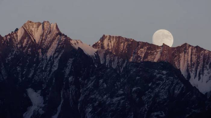 a full moon dropping low in the sky behind a reddish mountain range