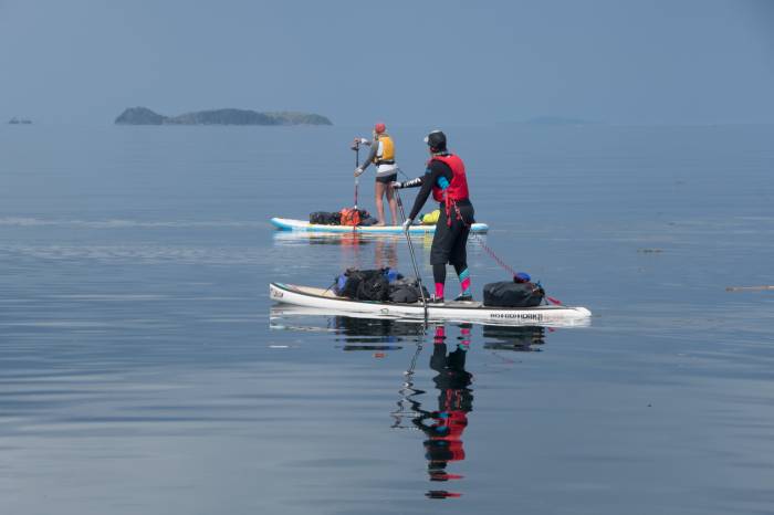 Two people headed out on a SUP expedition wearing Mustang Survival.