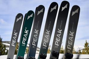 22/23 Peak Skis in Big Sky, Montana leaning against a fence and snowy backdrop