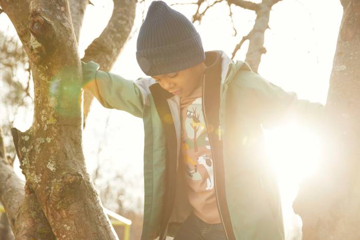 A young child in a beanie and green jacket climbing in a tree