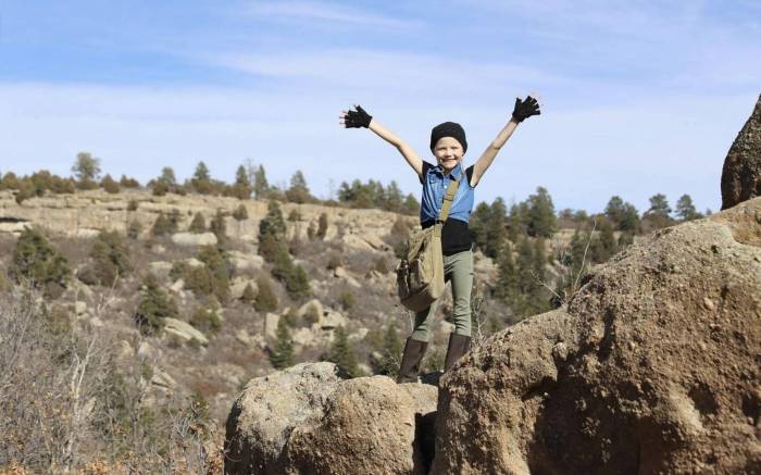 a kid standing with his arms outstretched on top of some rocks outdoors