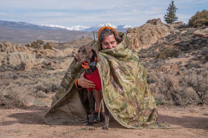 man hugging dog with army blanket