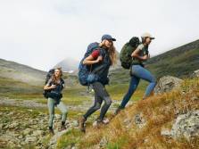 3 women wearing Fjallraven leggings while hiking up a grassy rocky trail
