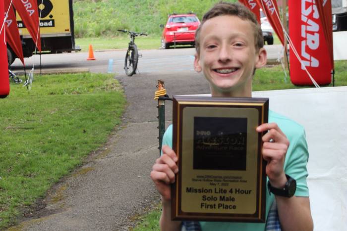 14-year-old boy smiling at the finish line with a plaque afterbeating out adult adventure racing teams