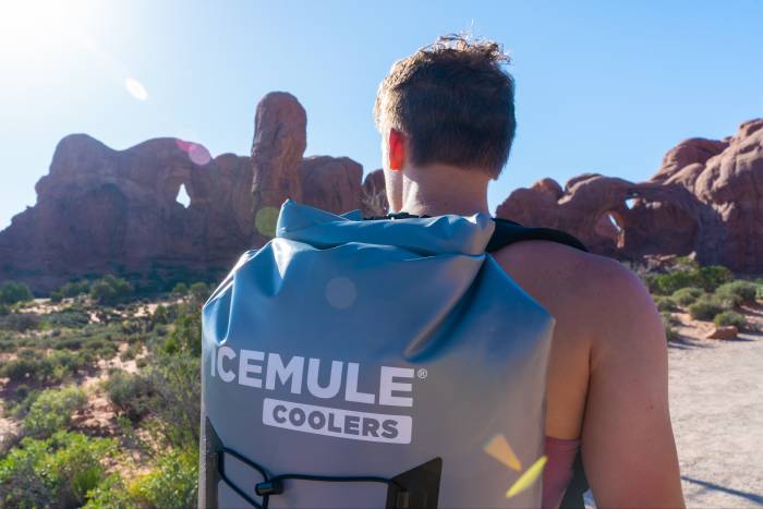 man carrying an ICEMULE cooler with some rock formations in the background