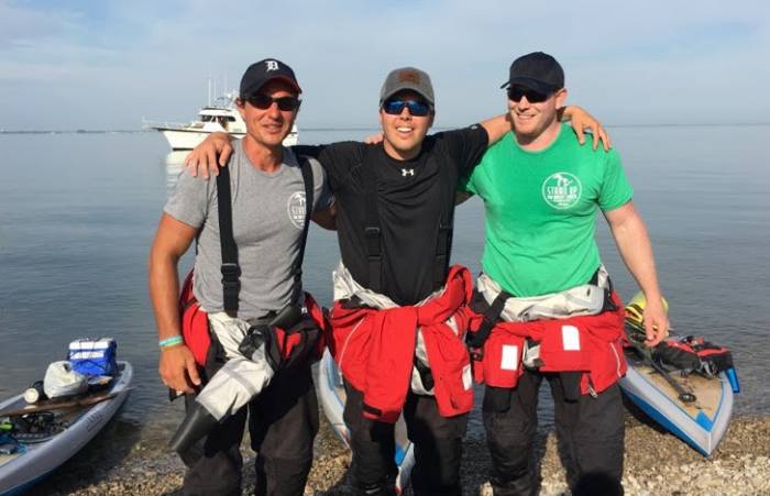 three friends wearing tee shirts and dry suits smiling after paddling across Lake Erie