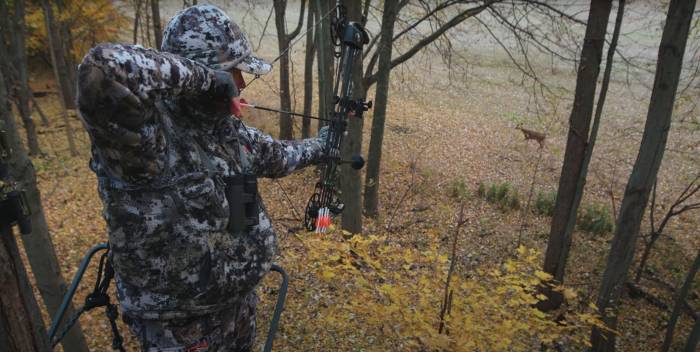 a man in cam draws a bow on a white-tail deer