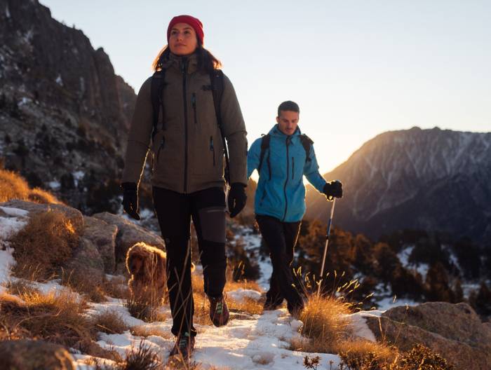 two people hiking with their dog while wearing Apricoat jackets