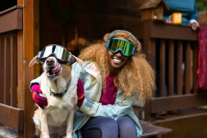 person and her dog wearing ski goggles in the snow