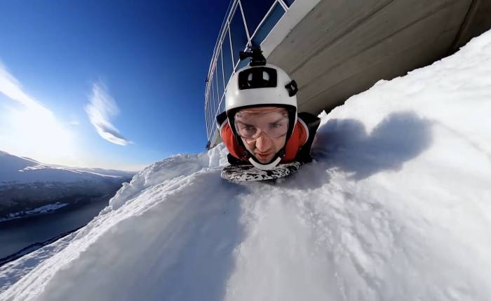 A wingsuiter in a helmet launching off a snowy cliff