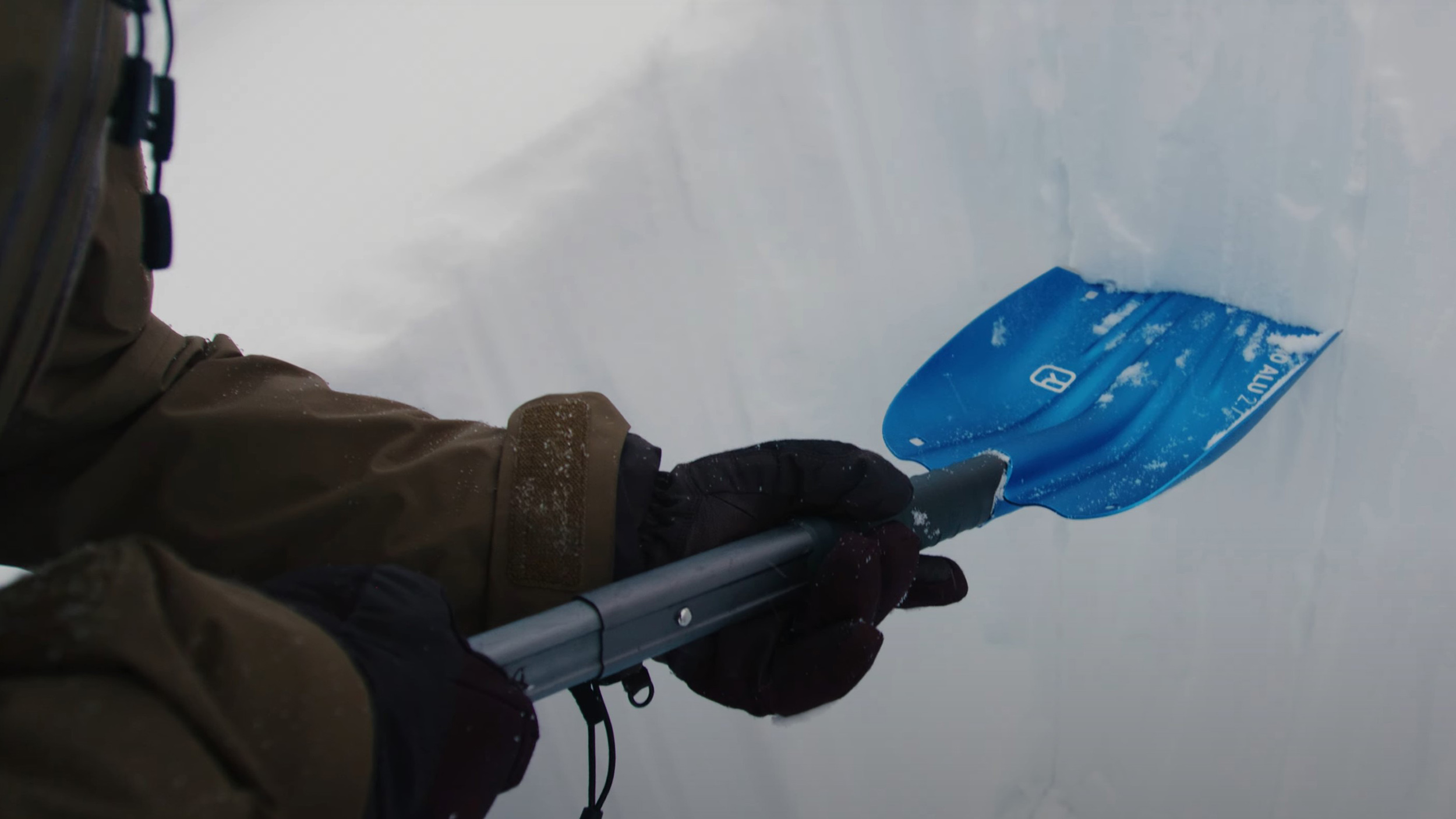 a close-up of a woman holding a snow shovel while digging a snow pit