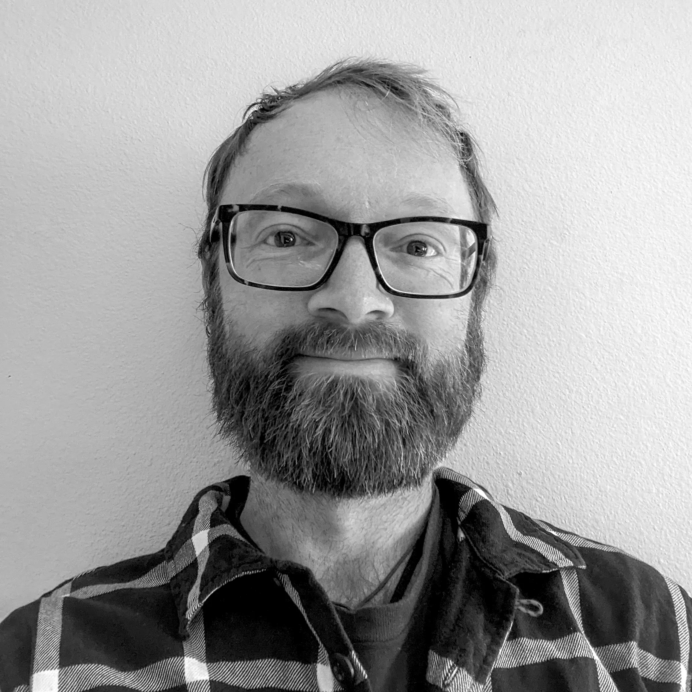 sam schild author headshot, a man in a plaid shirt wearing black rim glasses