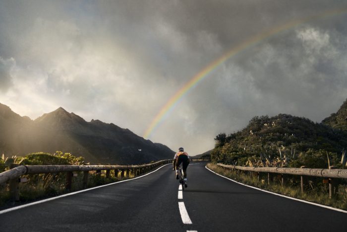 a road cyclist rides toward a rainbow