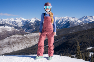 rider facing camera standing in ski bibs with mountain backdrop