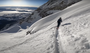 A skier ascends a snowy slope in the Teton range