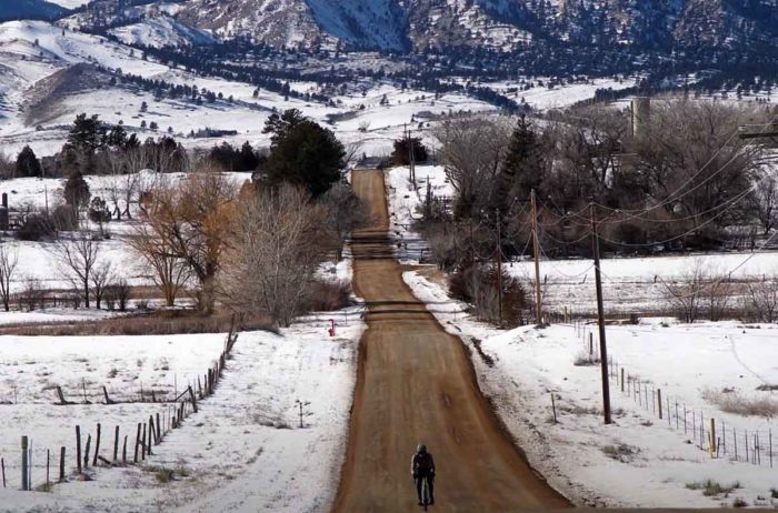 A gravel cyclist riding on a dirt road through snowy fields