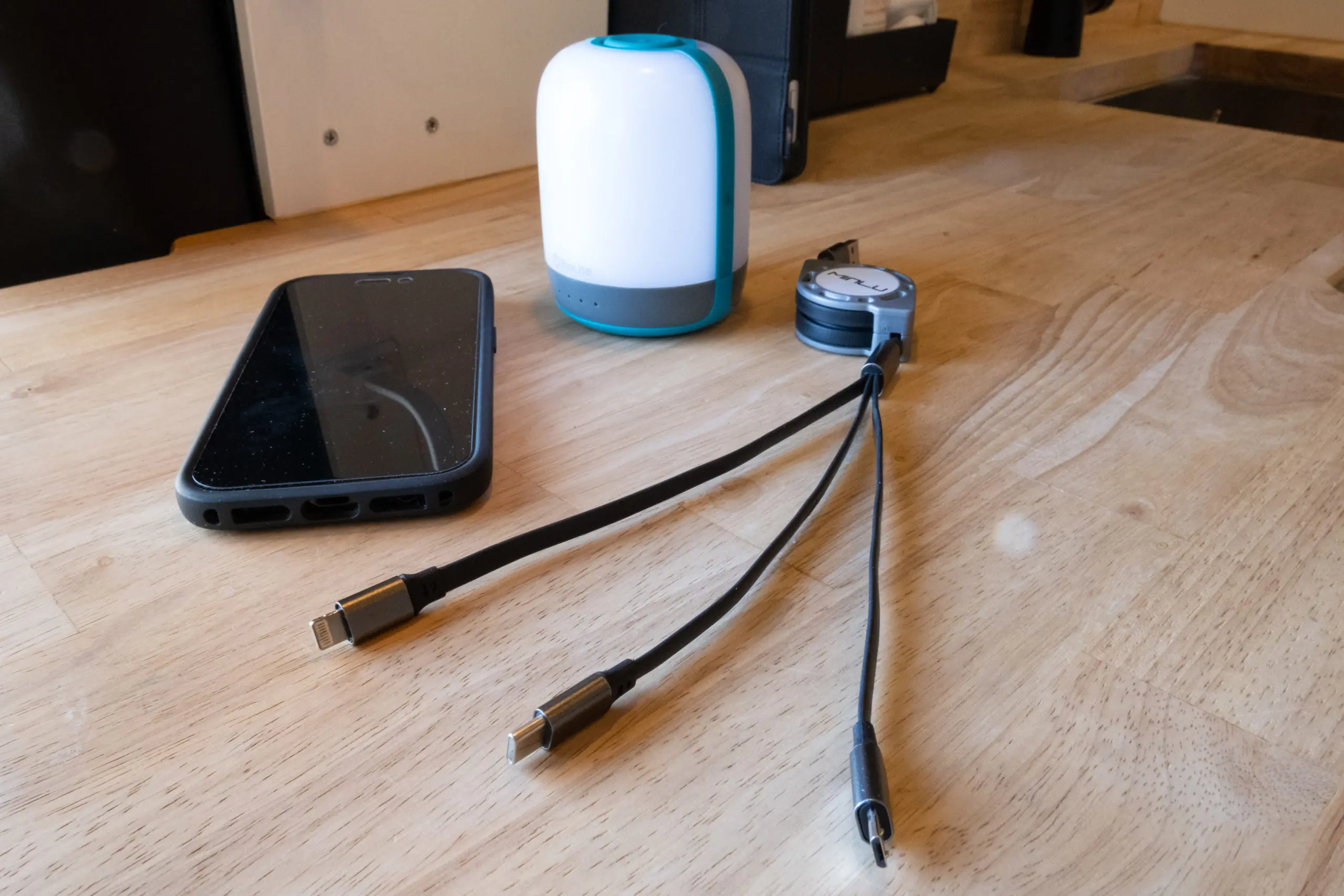 3 in 1 Charging Cable Next to an iPhone and Camping Lantern in a Campervan