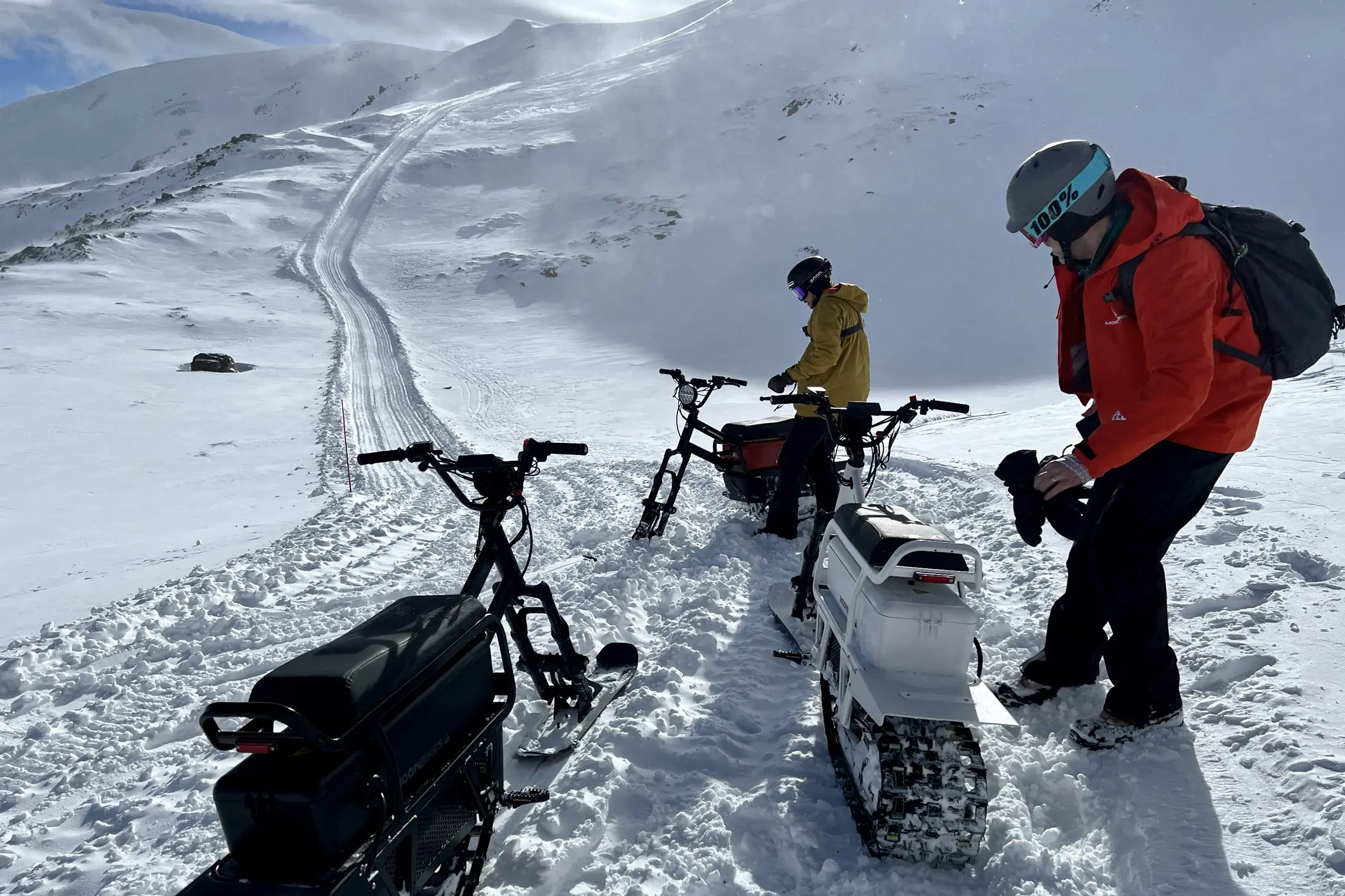 Three MoonBikes parked in snow with two humans.