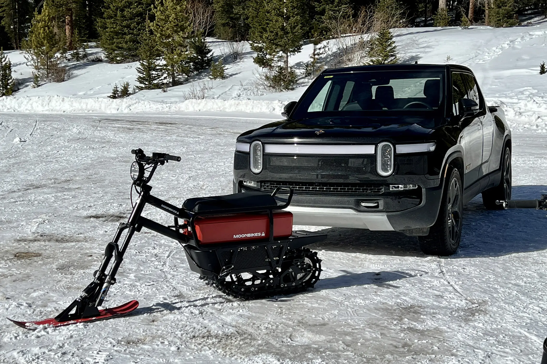 MoonBike parked on snow in front of a Rivian truck