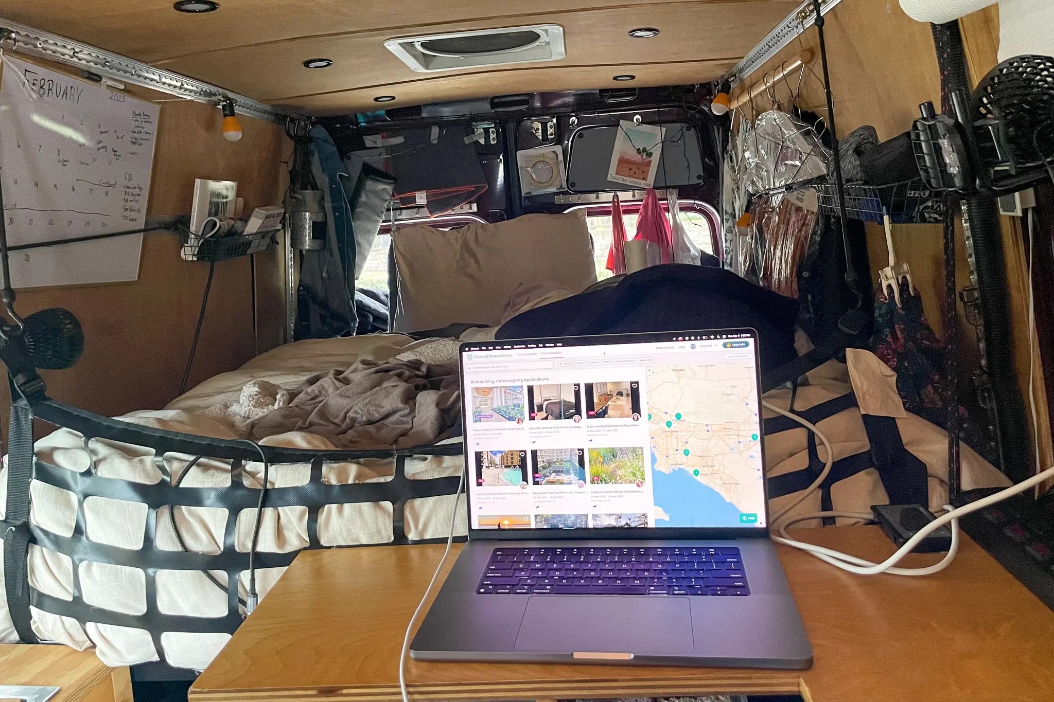 Interior of vanlife camper showing desk with laptop in front of bed
