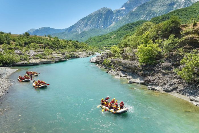A group of four yellow rafts floating among the rocks on the crystal clear, blue-green water of Vjosa river, Albania.
