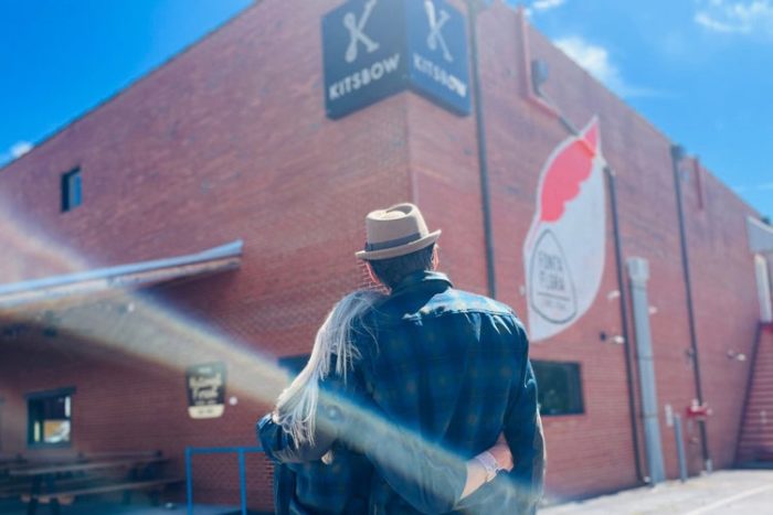 a man and woman embrace in front of the kitsbow factory