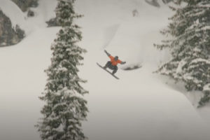 a man snowboards on a snowy hill with a pine tree in the foreground