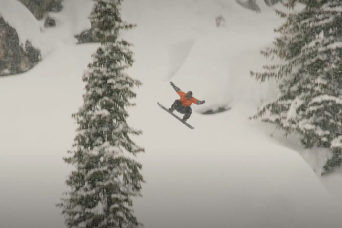 a man snowboards on a snowy hill with a pine tree in the foreground