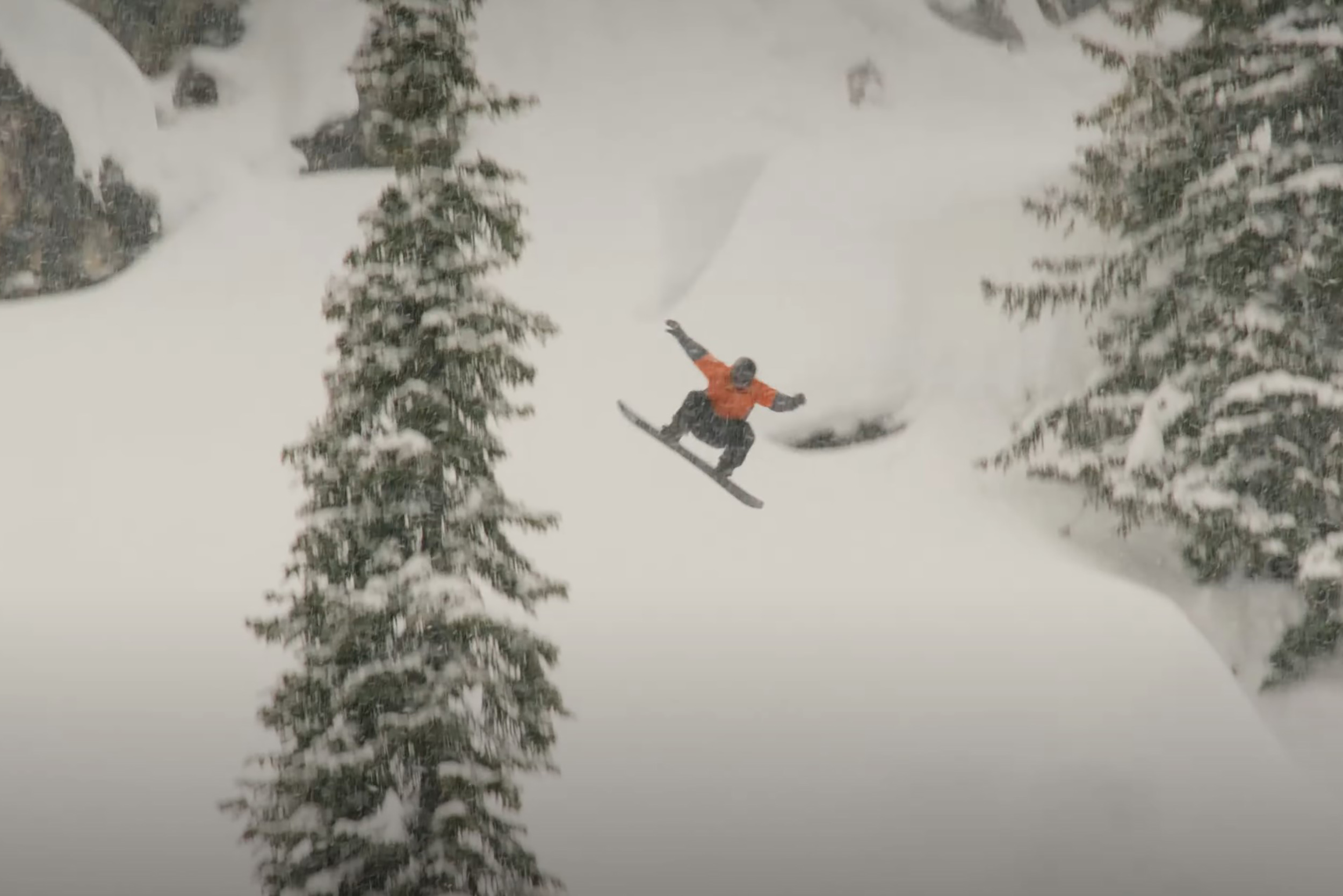 a man snowboards on a snowy hill with a pine tree in the foreground