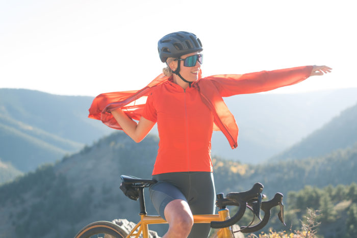 A woman on a yellow bike with mountains in the background. She is wearing the Rab Cinder cargo bib shorts, jersey, and phantom jacket.