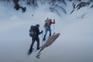 two backpackers wearing snowshoes climb a slope