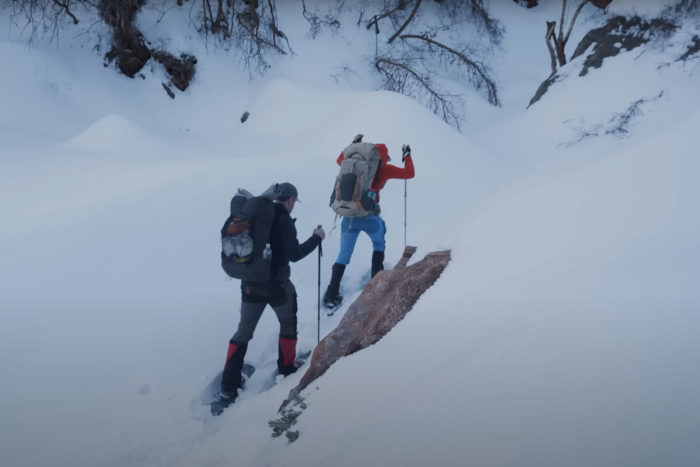 two backpackers wearing snowshoes climb a slope