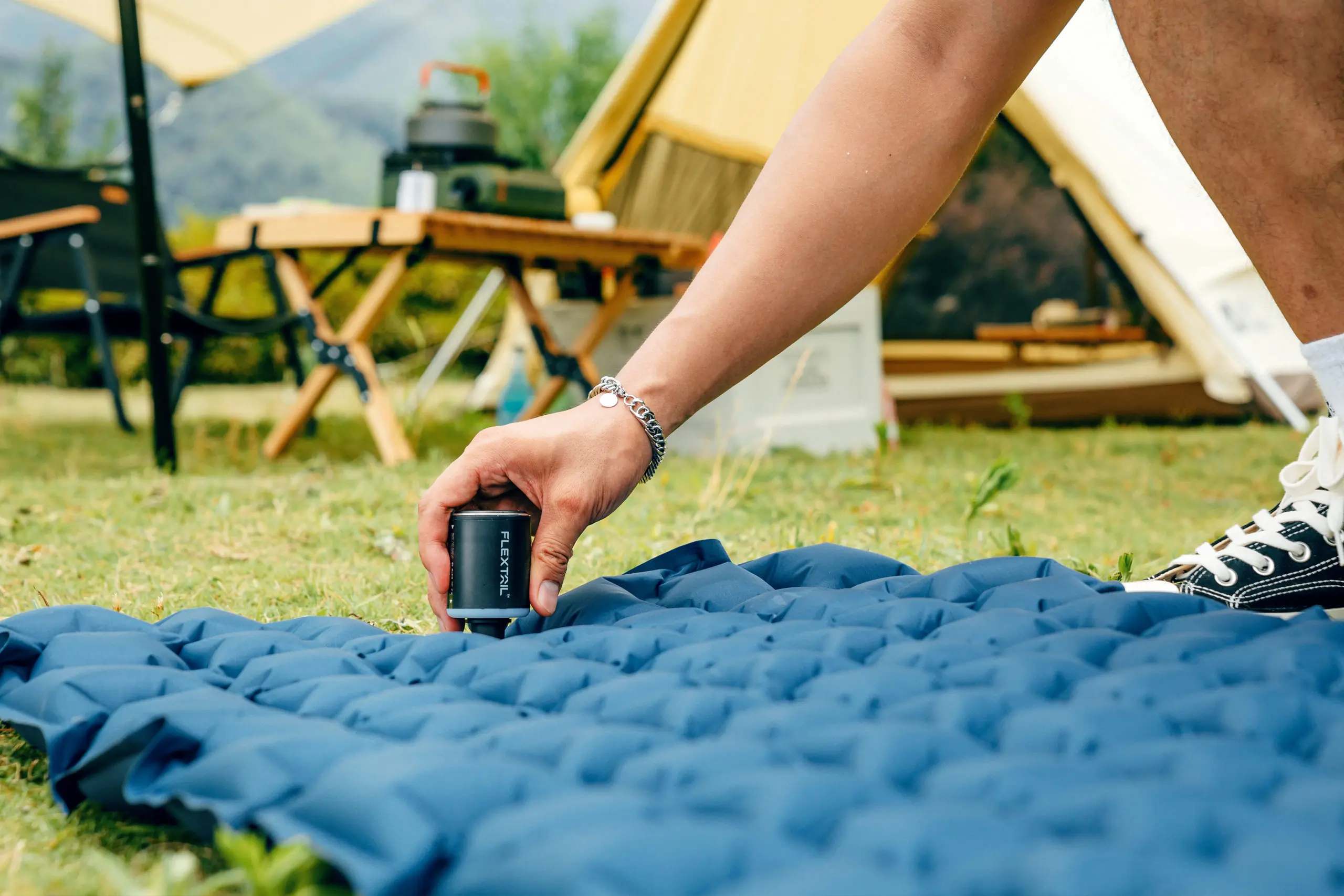 the FLEXTAIL TINY PUMP 2X inflating a sleeping pad with camp set up in the background