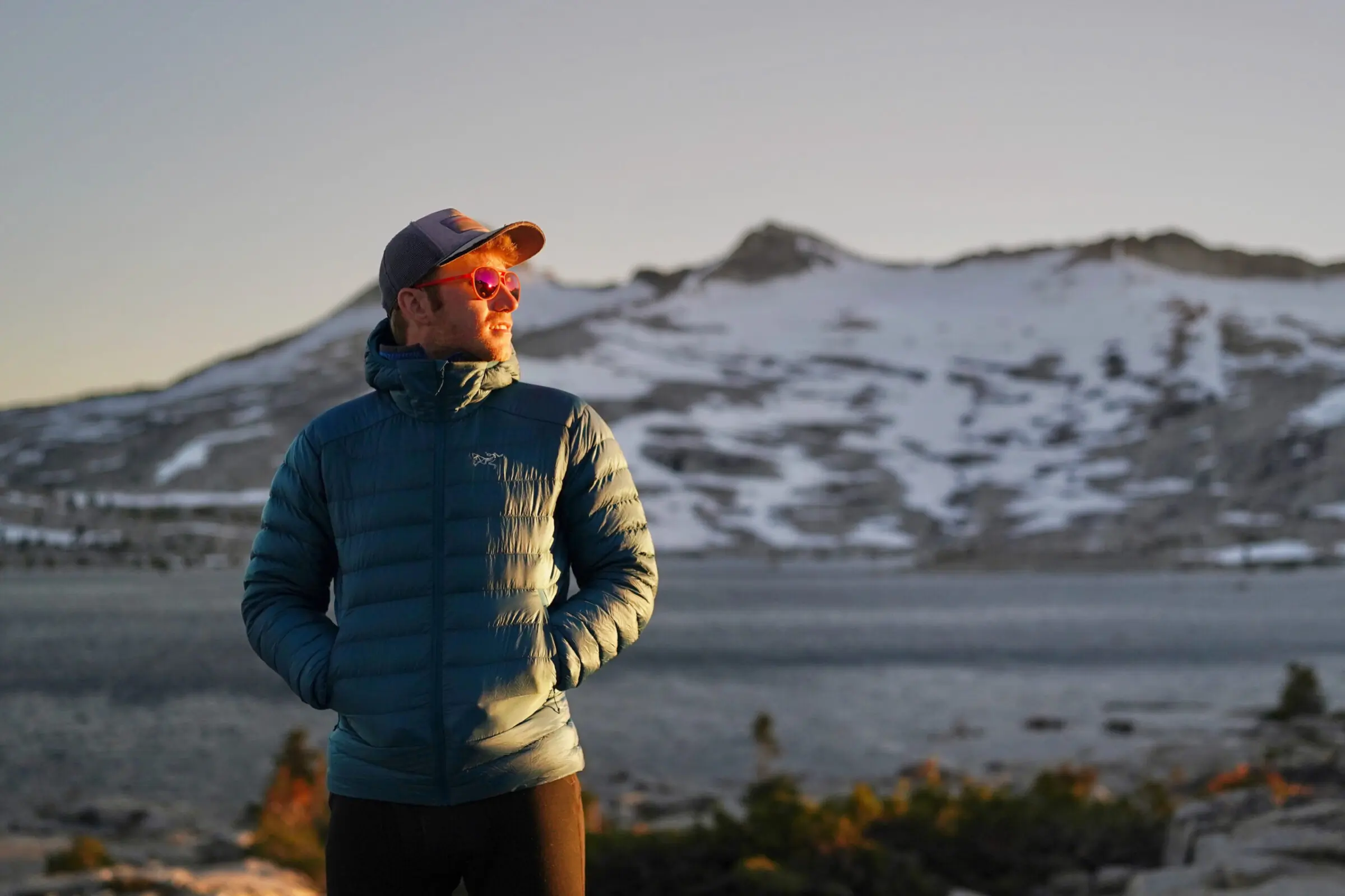 A man stands in front of a mountain range while wearing a down jacket