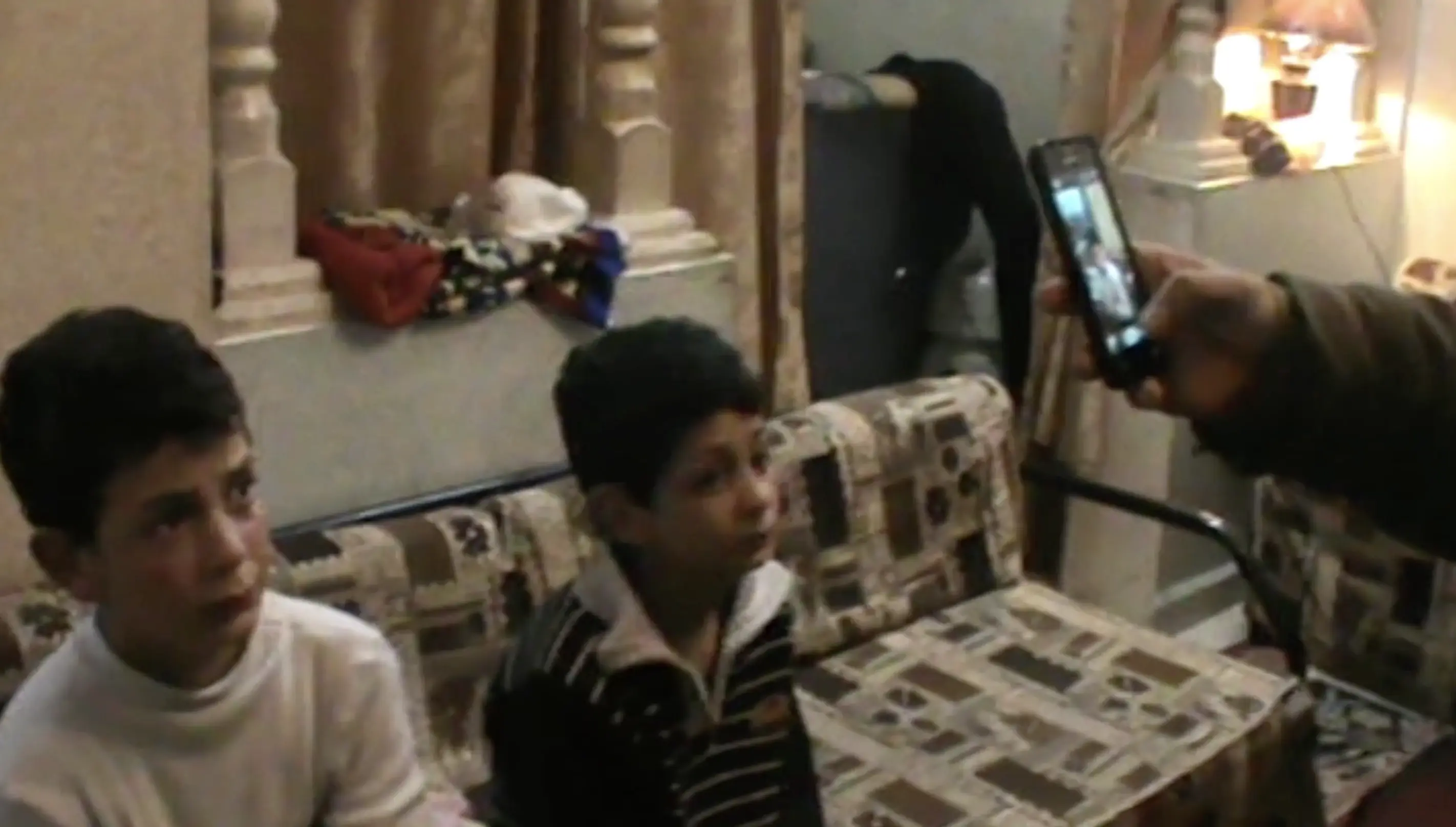 a soldier takes a cell phone photo of two children inside a home