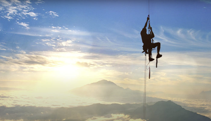 a climber ascending a rope as the sun sets