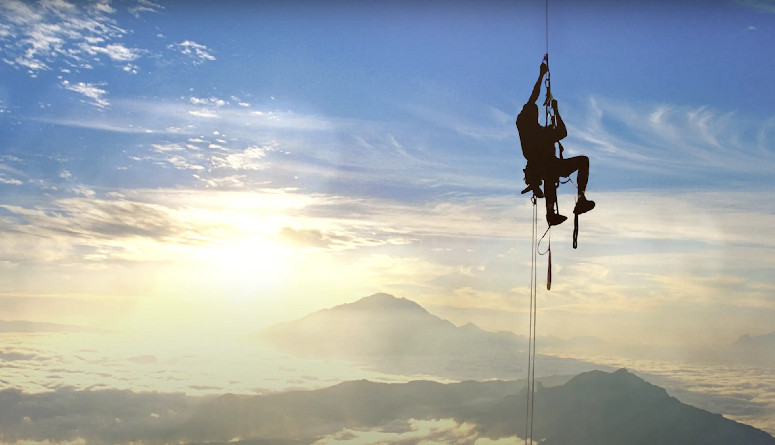a climber ascending a rope as the sun sets