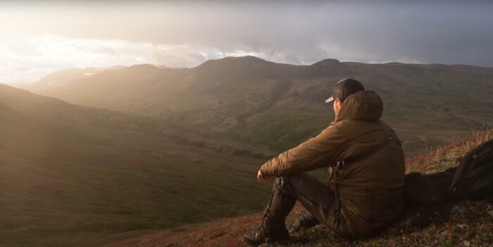 a man sits on the ground and watches the sun peak over a mountain range