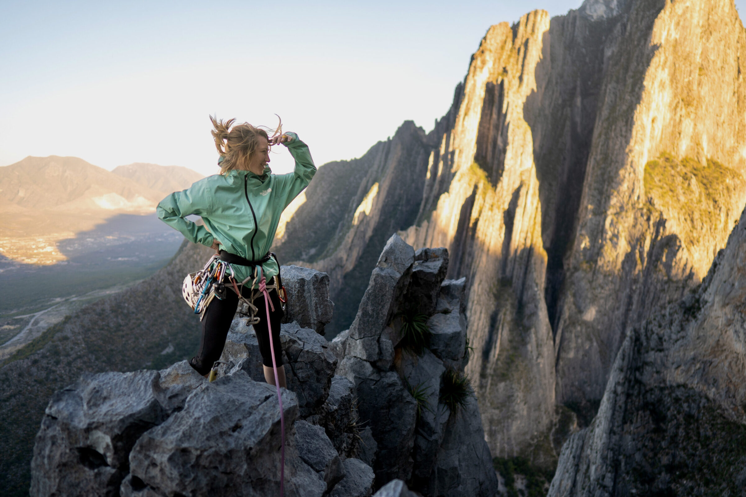 Woman wearing a windbreaker jacket on top of a mountain while rock climbing