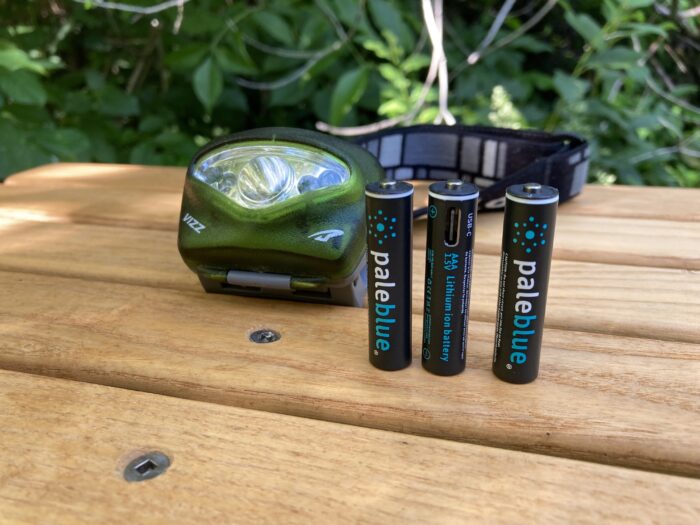 Pale Blue Earth AA and AAA rechargeable batteries next to a headlamp outside