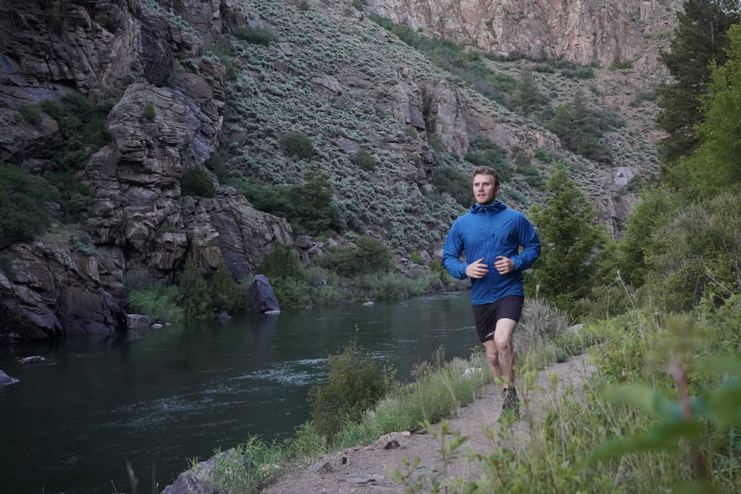 Man runs down a trail wearing a blue windbreaker jacket
